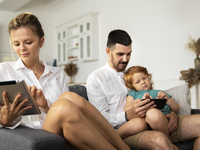 Parents and a child sit in the living room, each using their mobile phones with no interaction between them