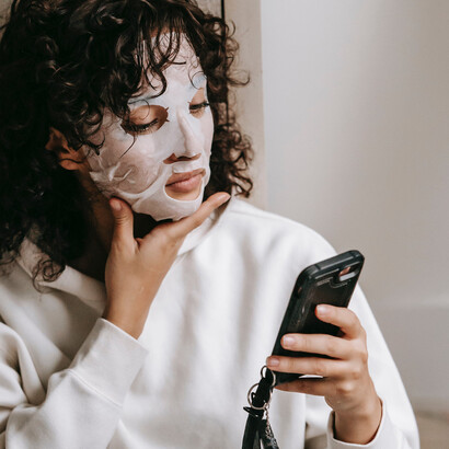 Jovem leitora escuta audio livro no celular enquanto segue sua rotina de skincare
