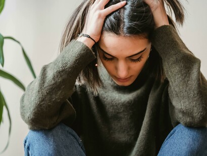 Upset woman sitting on a chair with her knees drawn close, struggling with negative thoughts
