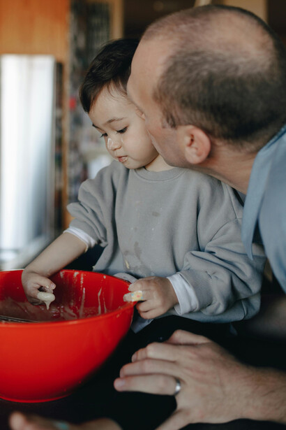 A cena de um pai brincando com seu filho enquanto cozinham ressalta como a afetividade e o envolvimento emocional fortalecem os laços familiares e promovem o desenvolvimento infantil