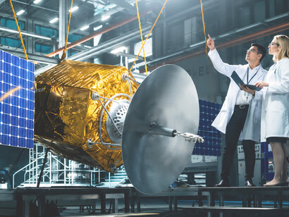 Engineers and technicians inspect a satellite assembly, using sophisticated instruments and tablet computers to support spacecraft development