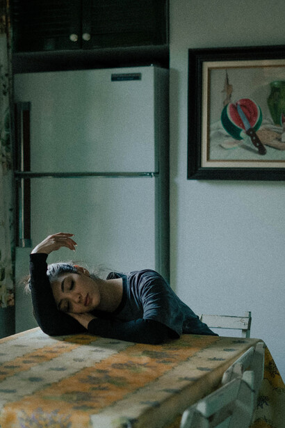A contemplative young woman seated alone in a dim apartment, symbolising urban loneliness and emotional pressure on women in the Middle East