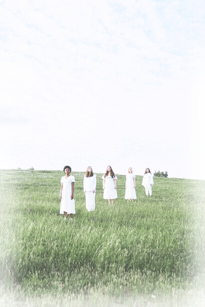 Five women stand in a diagonal line in a green field on a hill