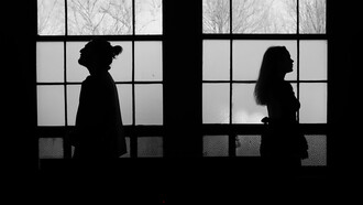 Two figures facing away beneath arched windows, symbolizing relational drift and the invisible space between partners