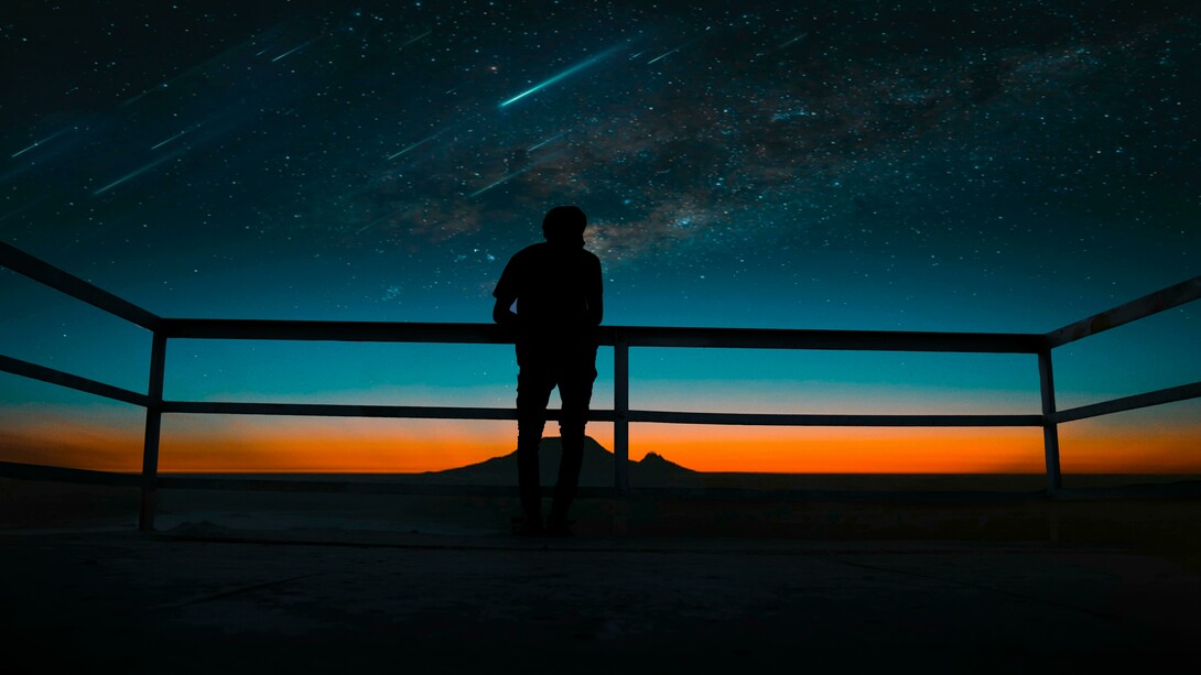 Under the night sky, a person gazes at shooting stars and meteors