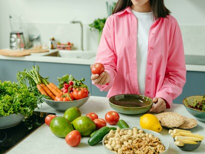 A person wearing a pink overshirt holding a tomato while preparing fresh ingredients for a healthy meal