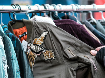 A person selecting a shirt from a charity shop rack, highlighting the growing trend of second-hand shopping and sustainable fashion