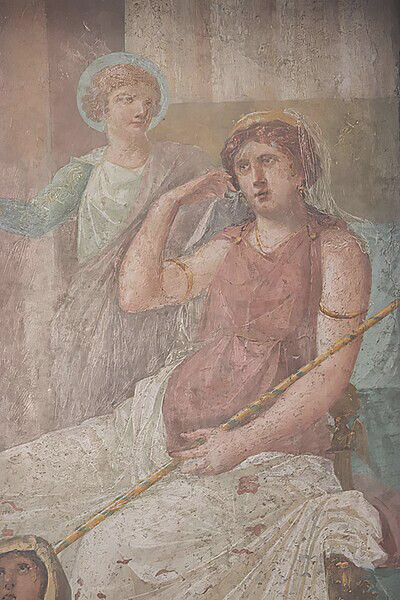 In the House of the Vettii VI 15,1 Pompeii, a depiction of Hera (Juno) adorned with a gold crown and holding a long sceptre sits on her throne, accompanied by Iris standing to her left, Italy