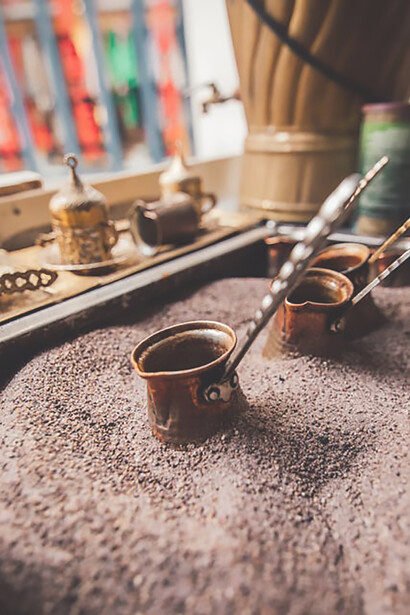 Experience the allure of Turkish coffee brewing in a copper pot on the sand through this captivating image