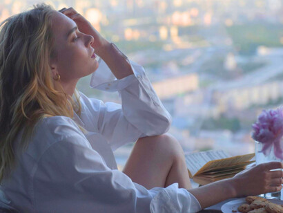 A woman looking over a hazy city skyline with distant eyes, representing the quiet ache of urban loneliness