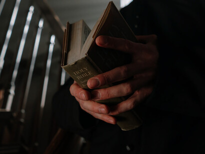 The priest's hands cradle the holy book, a remnant from a distant era