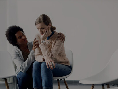 A compassionate African American woman supports a distraught woman before a group therapy session, promoting self-awareness and personal transformation