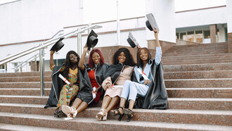 A picturesque scene unfolds as a group of young African American female students dons black graduation gowns against the backdrop of a campus setting