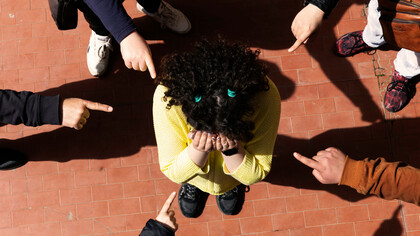 A young person wearing a garment is mocked and pointed at by classmates, experiencing bullying