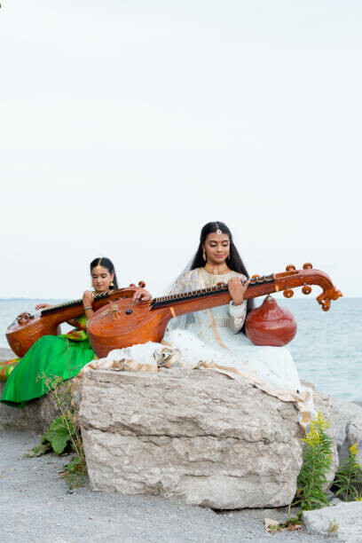 Two girls gracefully play the veena by Lake Ontario in Toronto, creating a serene and musical ambiance