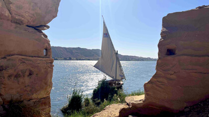 Gebel el-Silsila with rock-cut loopholes overlooking the Nile, as a felucca sails past in Egypt