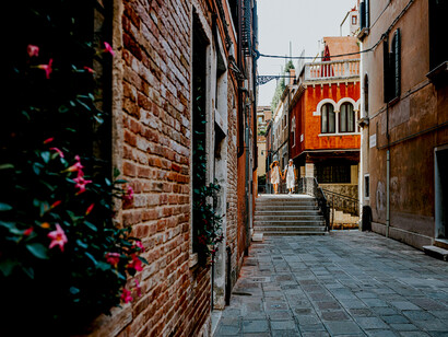 A charming Italian street lined with colorful buildings, flower-filled balconies, and narrow, winding lanes