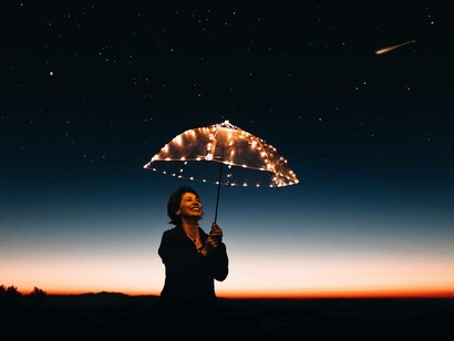 A woman holding a lit umbrella which is guiding her on her journey