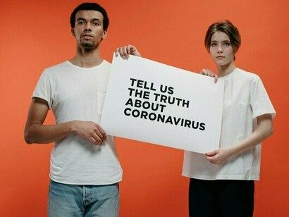 Two individuals holding a placard about COVID-19 truth, symbolising the social impact of misinformation and unanswered questions
