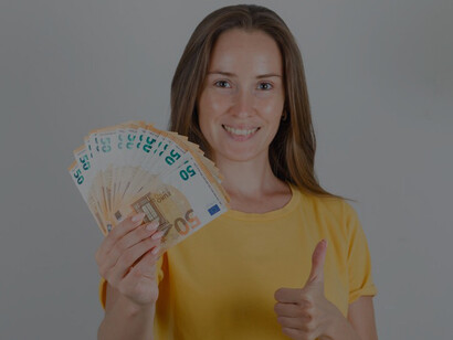 A cheerful young woman in a yellow t-shirt joyfully points at euro banknotes with a big smile on her face