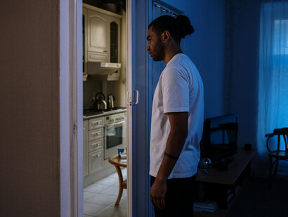 Calm apartment interior with a man in a white T-shirt standing near a sliding glass door under blue light