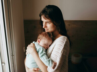 A woman holding a baby in her arms near a window