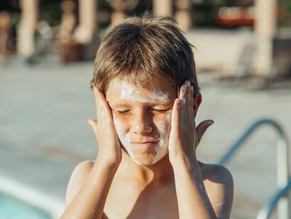 A boy rubs sunscreen on his face, as it is essential when going into the sun