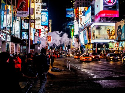 Rua repleta de outdoors e propagandas diversas. Campanhas de mídia paga não são apenas sobre apertar botões ou configurar palavras-chave. Elas envolvem contexto, timing, narrativa e propósito. E ainda que a IA evolua rapidamente, ela não substitui a sensibilidade humana de entender o negócio, antecipar movimentos do mercado ou adaptar uma mensagem ao tom certo para um público específico