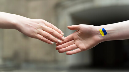 Two people shaking hands, one with a Ukrainian flag on his wrist