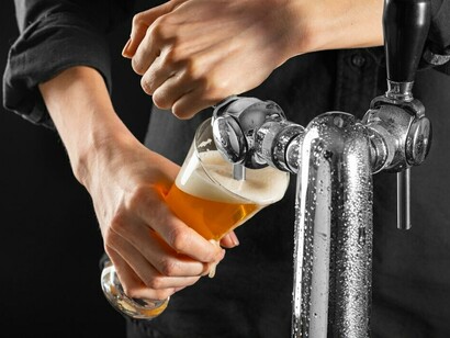 A bartender expertly pours beer from a keg into a glass, creating a perfect pour with a smooth, foamy head