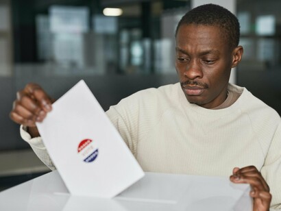 A young man putting his vote in a ballot box, a contrast to the growing issue of political apathy, particularly among the youth, who often feel their voices are unheard, contributing to a steady decline in voter turnout and engagement