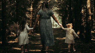 Hand in hand, they move forward — a quiet moment of safety and belonging beneath the trees