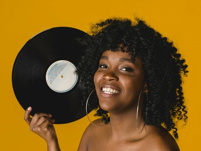 Africana posa com disco de vinil. O Afrobeats é a música pop da África Ocidental, mesclada com ritmos locais: essa mistura derivou em batidas tranquilas com vocais vibrantes, videoclipes com muita cor e beleza, e pura identidade negra. Antes estava englobado no mal-chamado estilo *world music*, um conceito que difuminava a identidade e a voz africanas e de outros lugares do mundo. É o ritmo que conseguiu furar a bolha das paradas de sucesso na Europa e no resto do mundo, e Rema é a prova disso: cantou na cerimônia da Bola de Ouro para milhões de pessoas