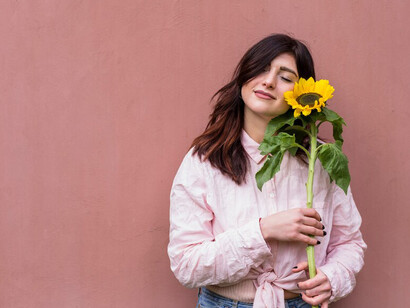 A woman gently holding a fresh yellow flower near her face, symbolizing self-love, authenticity, personal growth, and the freedom to embrace her uniqueness and the possibility of failure