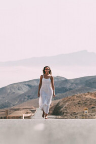 A woman walking on a road near hills under a cloudy sky, smiling, symbolizing her healing journey, spiritual warfare, and overcoming trauma, embodying peace and purpose