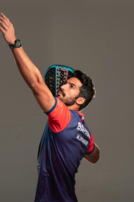 Athletic padel player getting into position for a shot on an indoor glass court