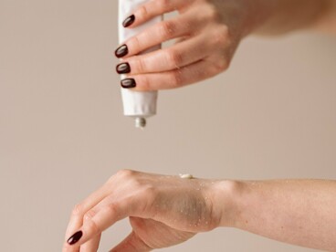 A hand dispensing a small amount of cream onto another hand, representing the balance between using enough product to support the skin and avoiding unnecessary excess