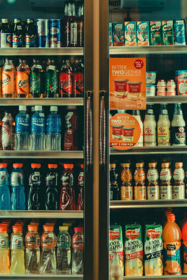 Assorted soda cans neatly arranged in a refrigerator display, showcasing the variety of sugary, ultra-processed drinks