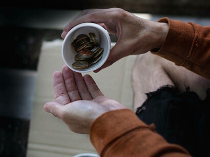 Bicchiere per l'elemosina contenente monete in procinto di essere versate sulla mano