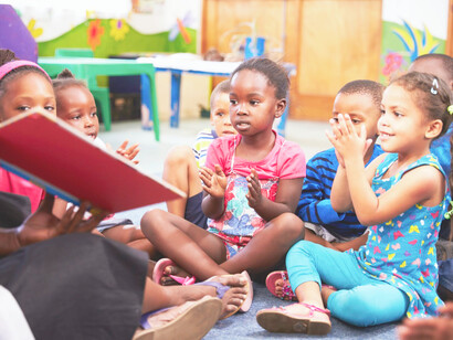 Seven children of color being read a book during kindergarten