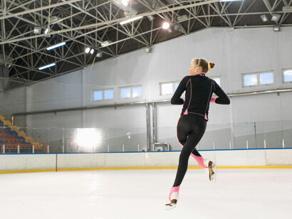 A young skater in a pink and black bodysuit glides across an empty ice rink under a focused spotlight