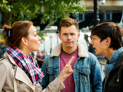 A young man intervenes in a heated political argument between two people, attempting to calm the situation