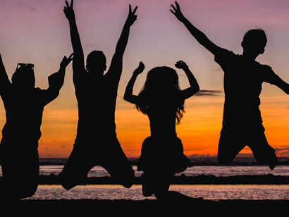 Silhouettes of people raise their hands in joy while enjoying the sunset during golden hour