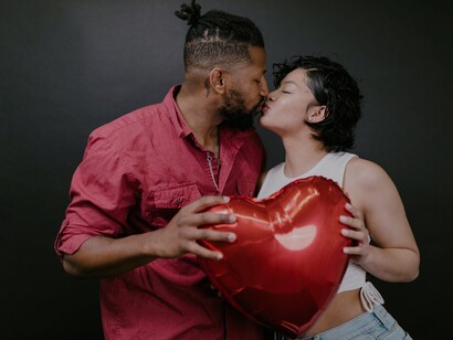 Casal beijando-se enquanto segura um balão vermelho em forma de coração