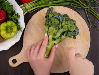 Fresh broccoli on a cutting board, vibrant bell peppers arranged on a plate, and crisp green onions with ripe tomatoes set against a rustic wooden background