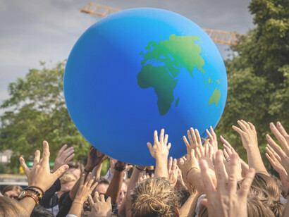 A diverse crowd gathers during a climate protest, raising a giant Earth globe as a symbol of environmental unity and collective responsibility in Berlin, BE, Germany