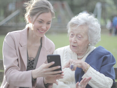 A joyful senior mother and her adult daughter happily using a smartphone together.
