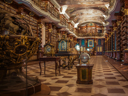 The grand Baroque Library of the Klementinum, Prague, lined with ancient books, ornate balconies, globes, and painted ceilings, representing the centuries-old pursuit of knowledge