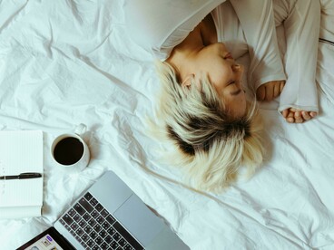 A student sleeping on a bed near a laptop and a cup of coffee after studying