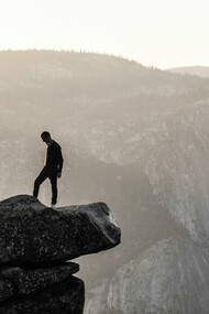 A man standing at the top of a rock mountain seemingly reflecting on life